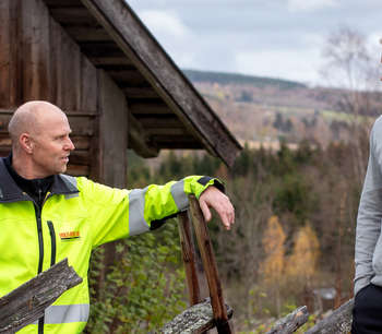 To personer snakker sammen foran et trehus