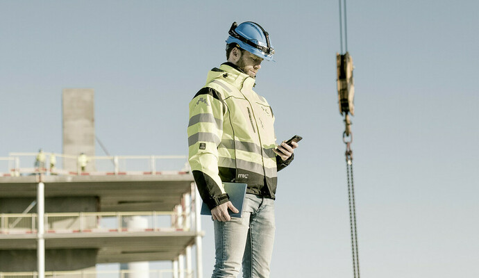 Person på byggeplass, ser på mobil