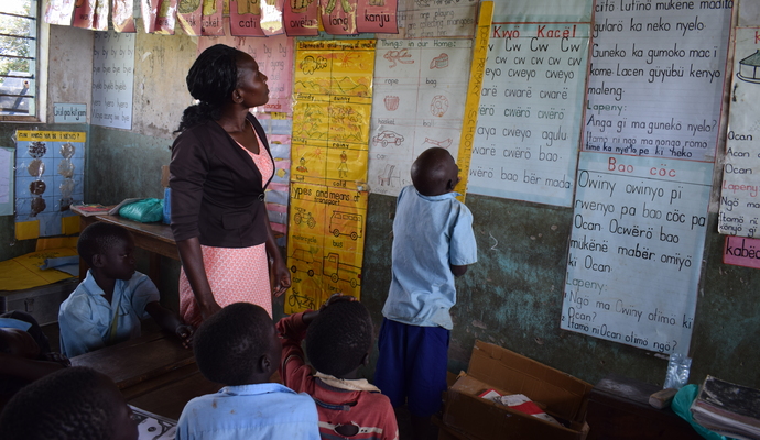 Gutt i Uganda leser med lærer på tavle