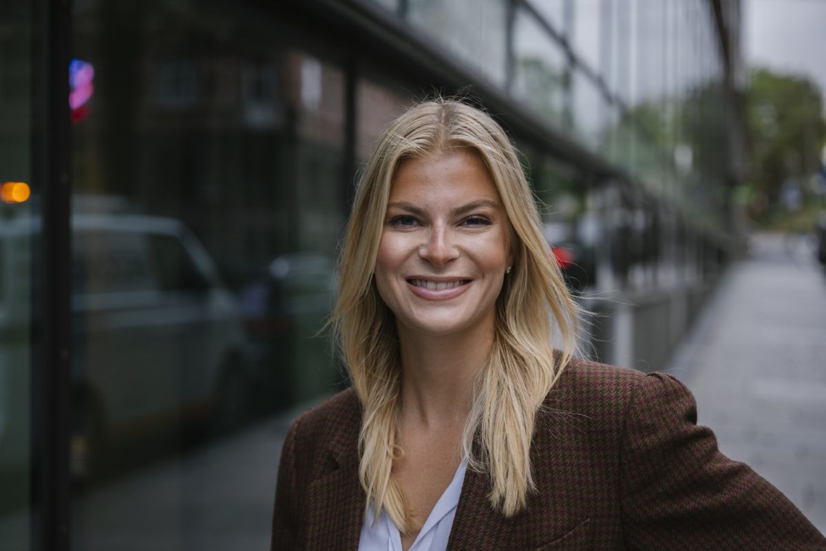 Hedda Berg står foran et kontor og smiler